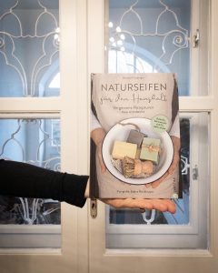 Frau mit seitlich ausgestreckter Hand, die das Seifenbuch von Barbara Freyberger hält